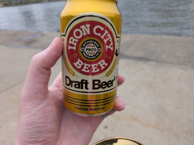 A pale hand holding a beer can. The can has the Iron City Beer logo under which it says "Draft Beer"